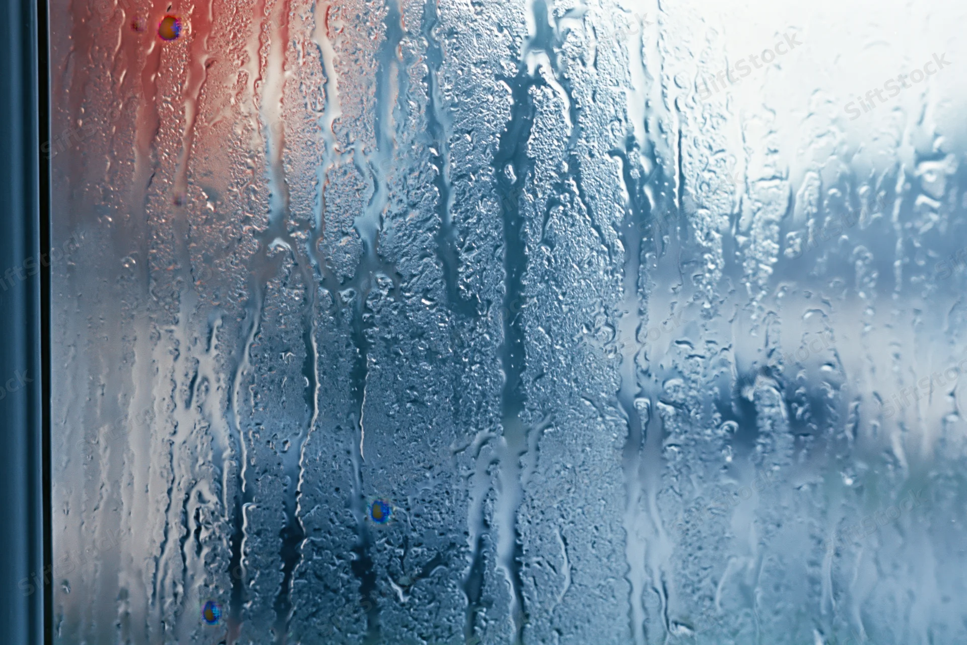 Close-up of condensation droplets and water streaks on a glass window surface