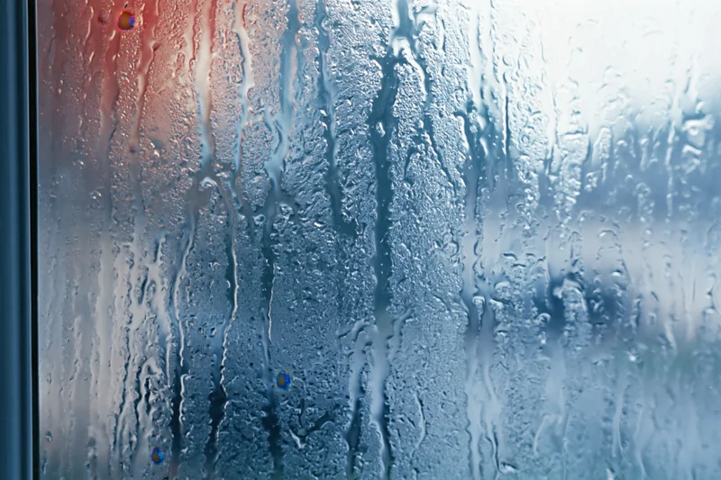 Close-up of condensation droplets and water streaks on a glass window surface