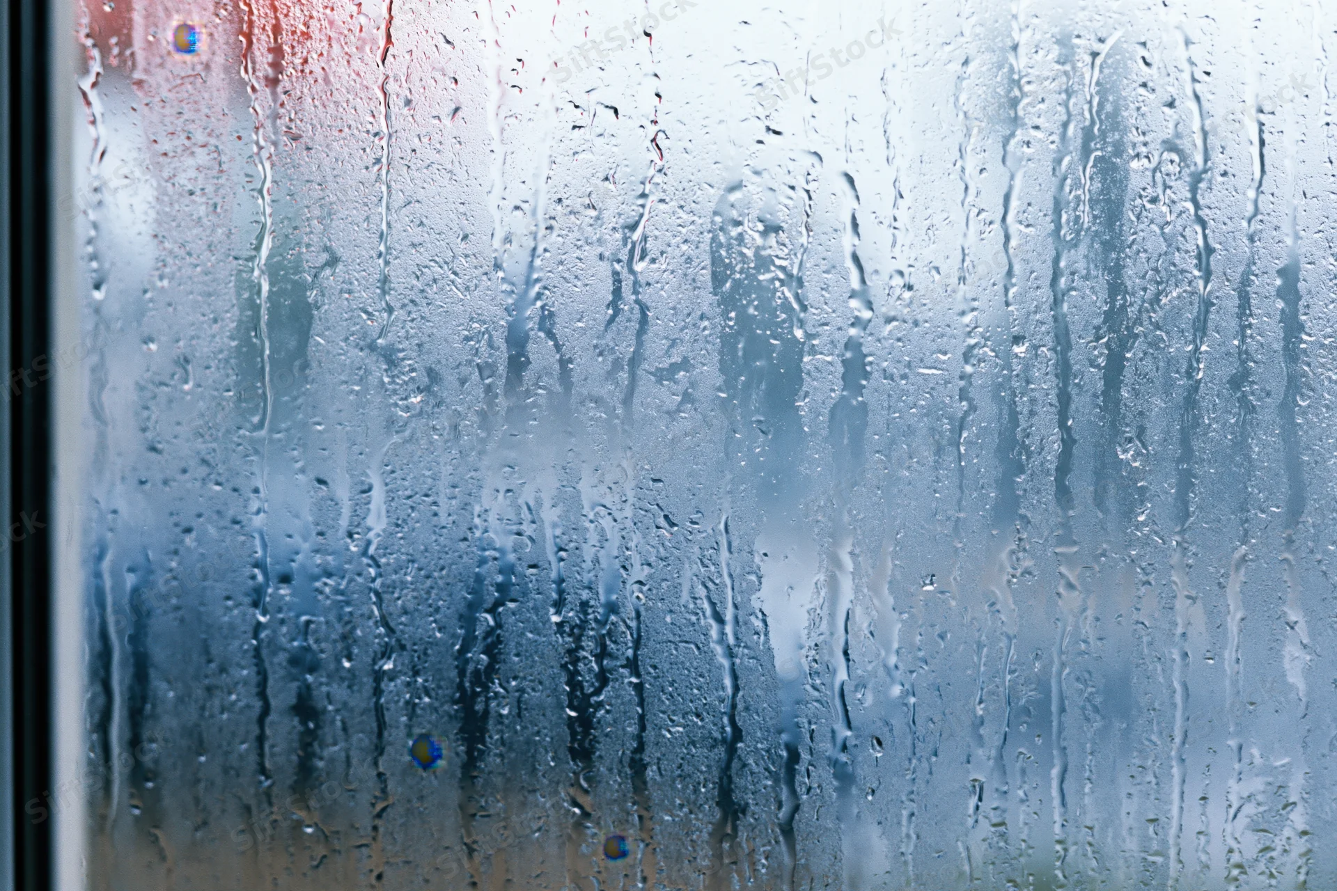 Close-up of condensation droplets and water streaks on a glass window surface