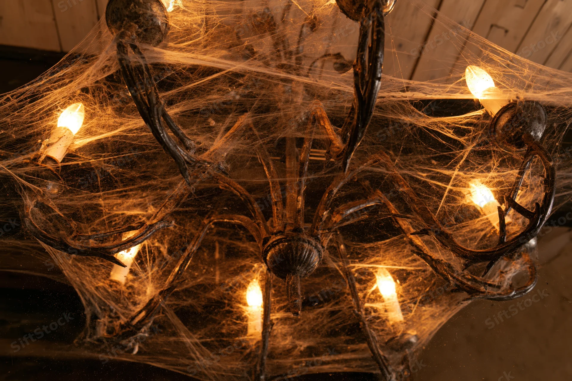 Old metal chandelier covered in spiderwebs with glowing candles viewed from below indoors