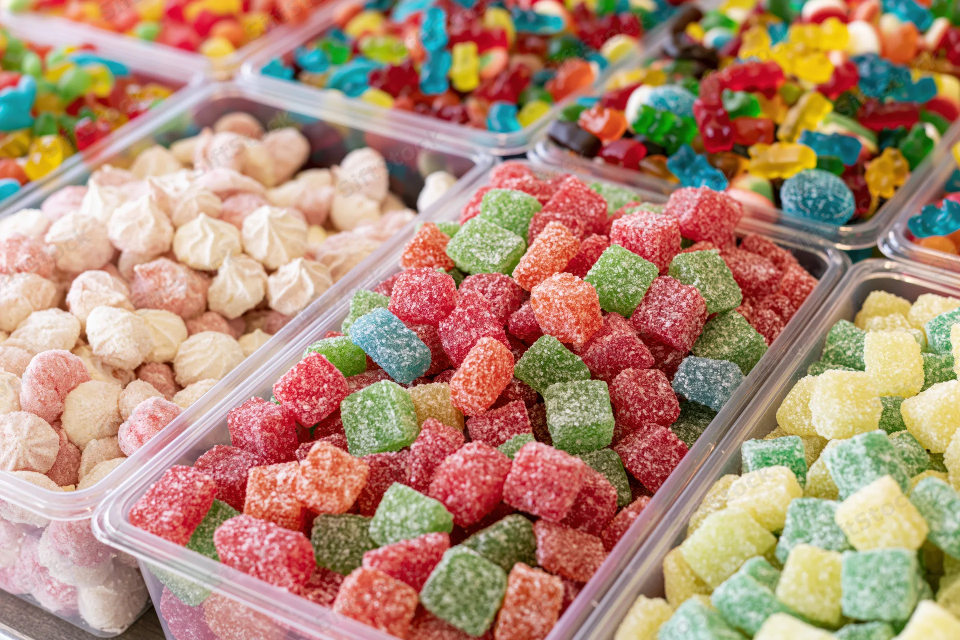 Colorful assorted gummy candies and meringues in clear plastic bins at a market stall display