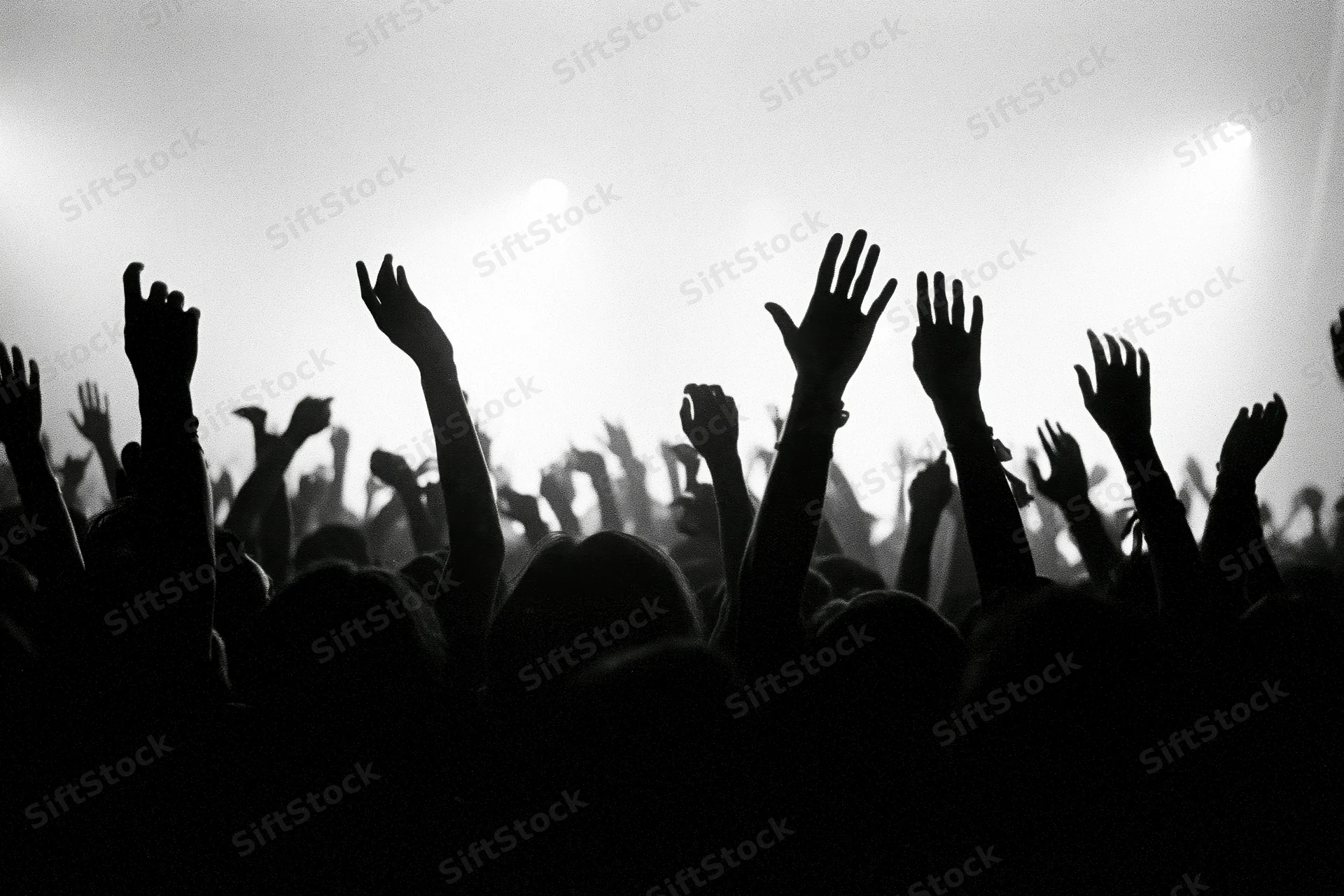 Silhouetted crowd with raised hands at a concert under bright stage backlighting