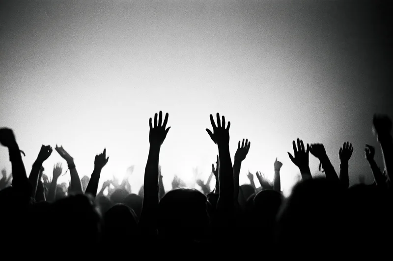 Silhouetted crowd with raised hands at a concert stage under bright backlighting