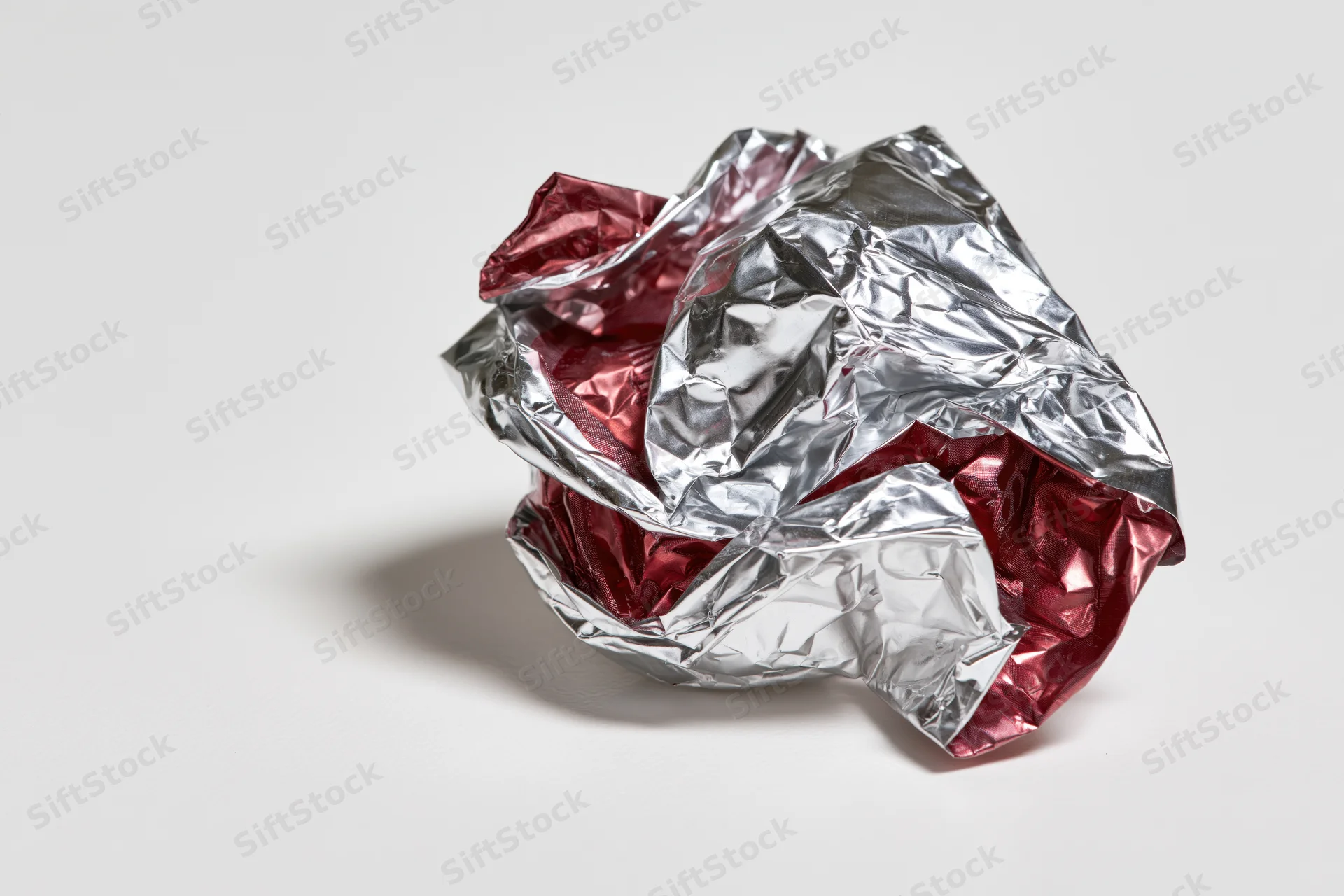 Crumpled silver and red metallic foil candy wrapper on white surface