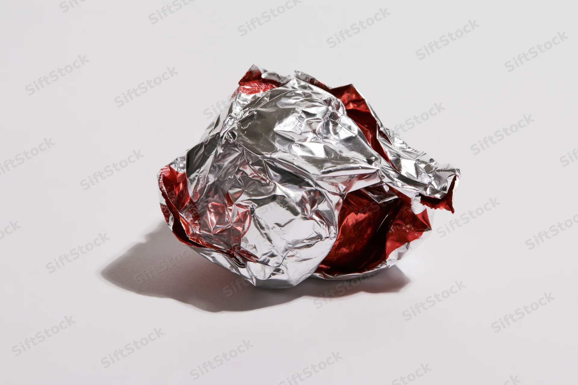 Crumpled silver and red metallic foil candy wrapper on white surface
