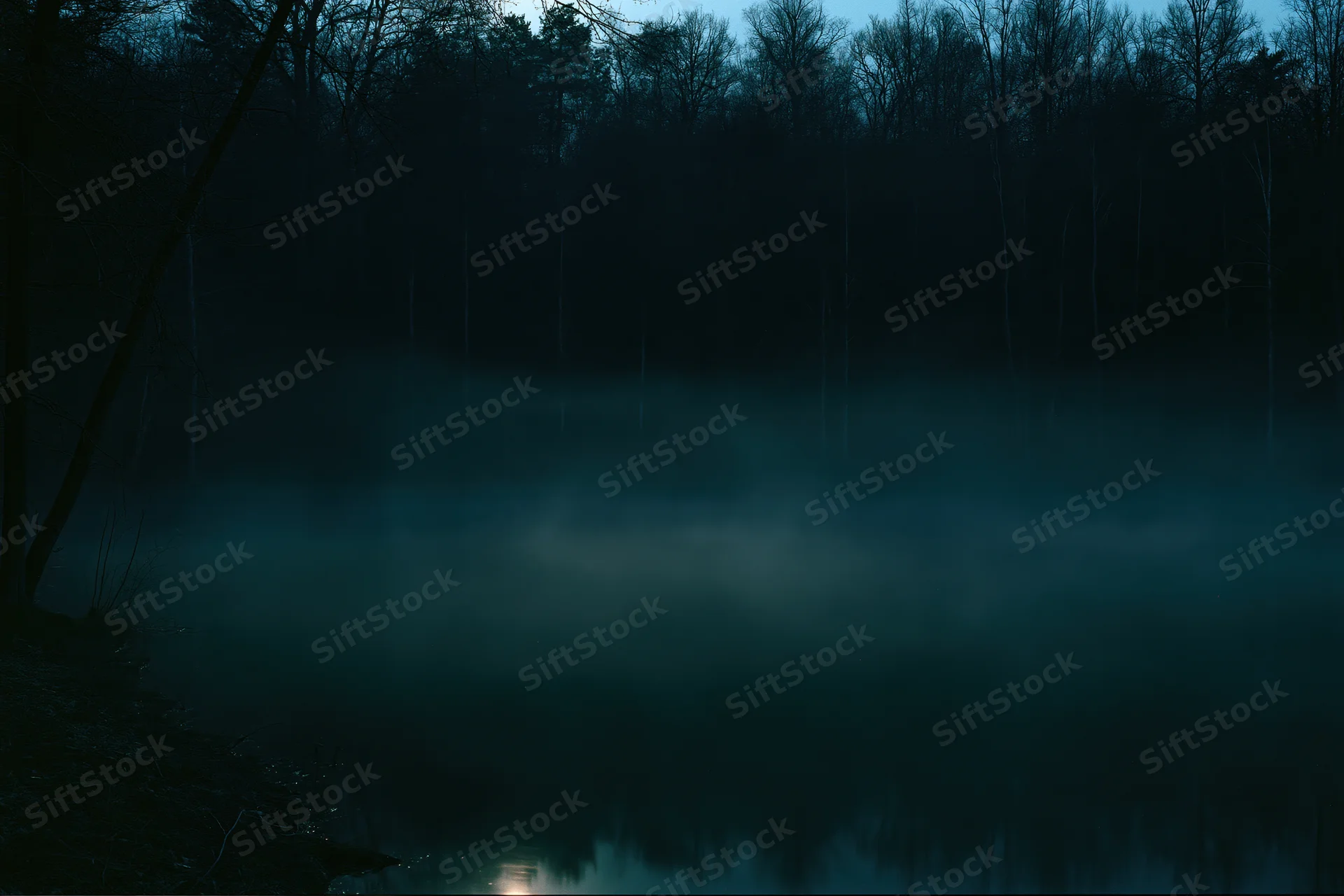 Mist rising over a still lake at night surrounded by dense dark woodland