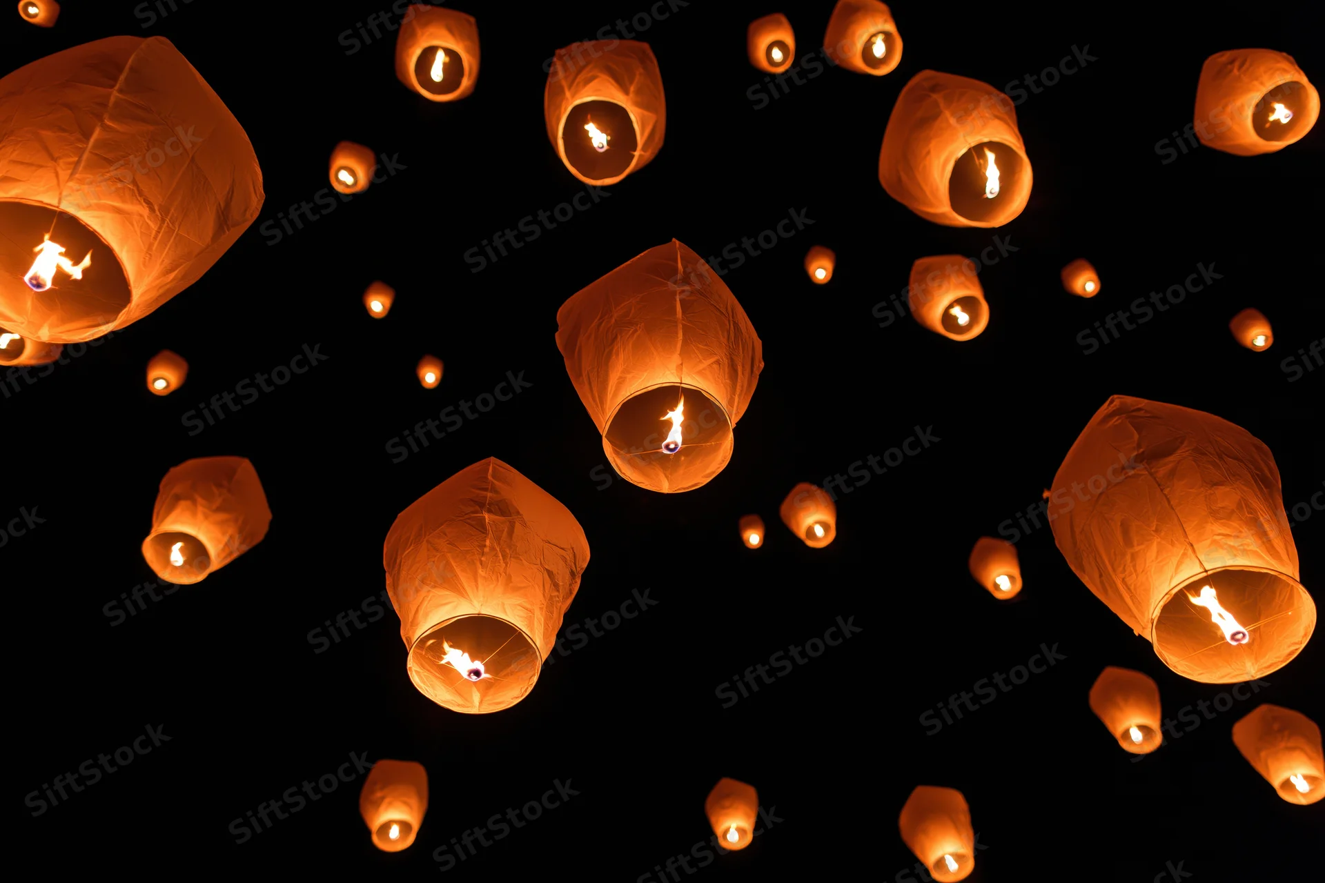 Paper sky lanterns floating upward against dark night sky