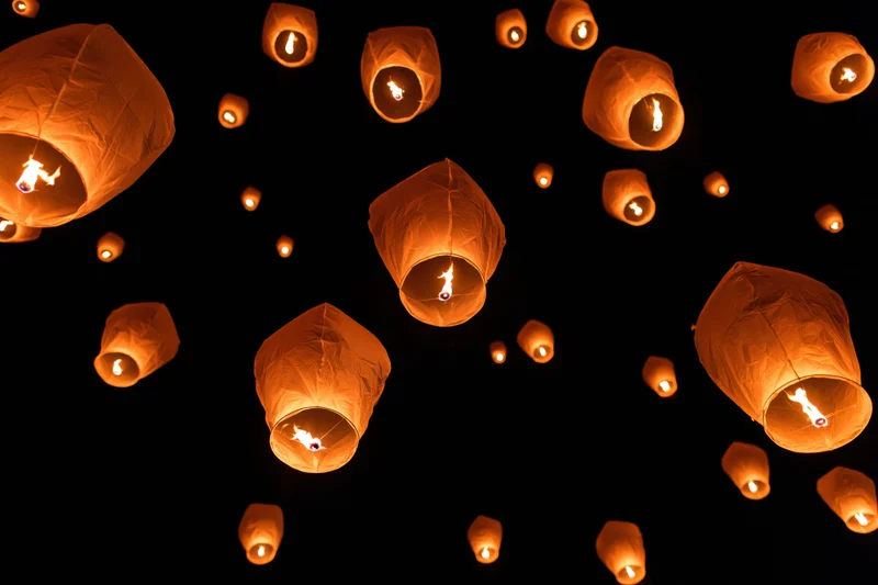 Paper sky lanterns floating upward against dark night sky