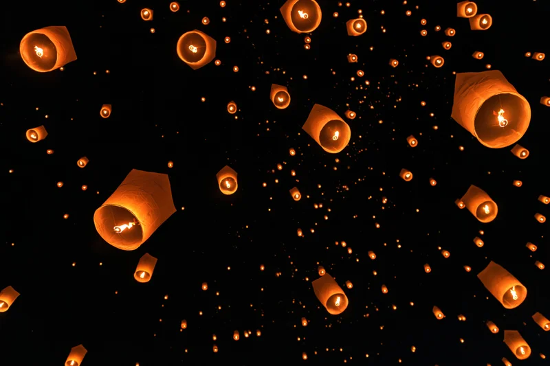 Paper sky lanterns floating upward in the night sky during a festival celebration