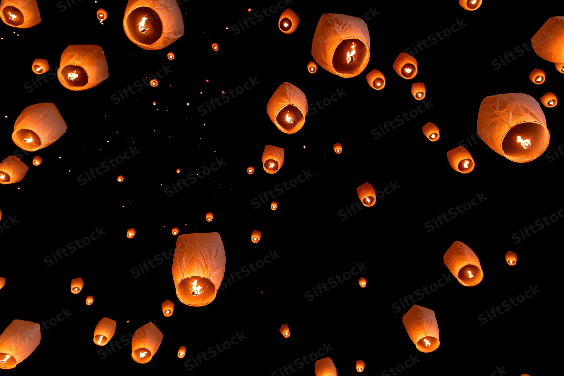 Paper sky lanterns floating upward against dark night sky