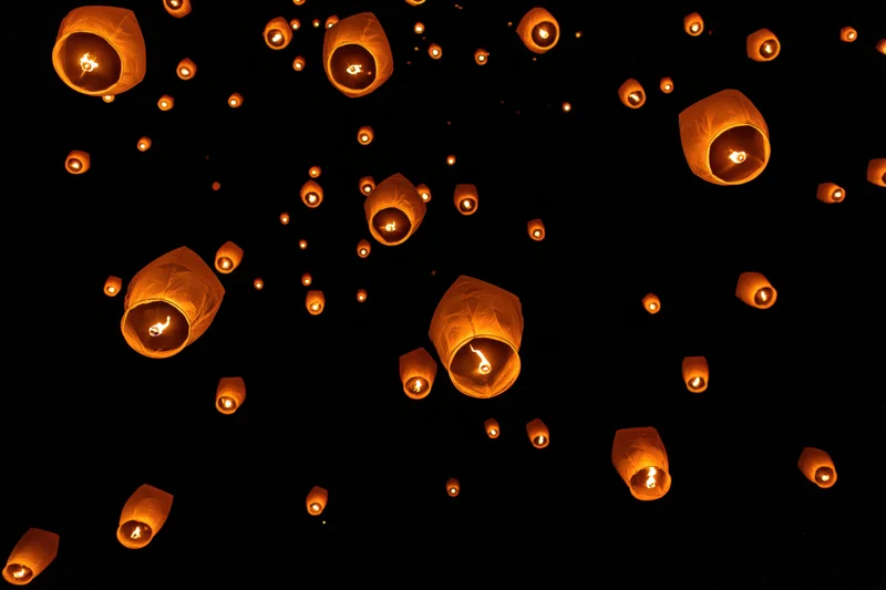 Paper sky lanterns floating upward against a dark night sky