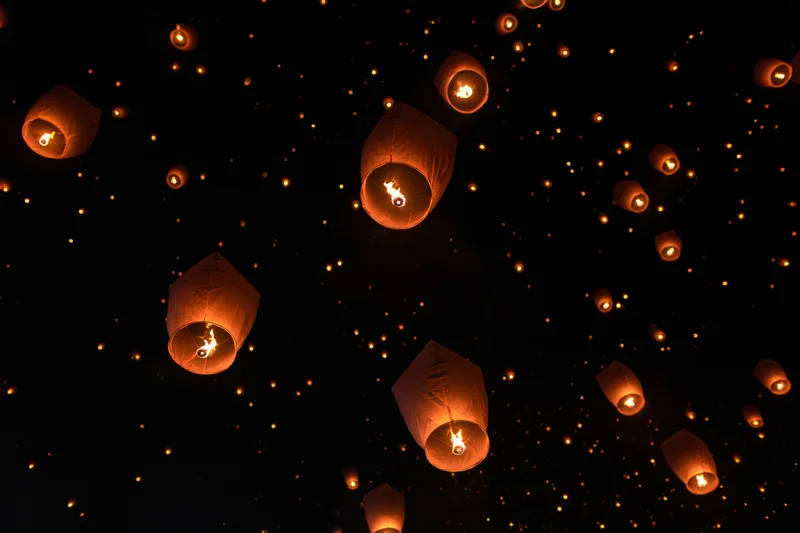 Paper sky lanterns floating upward into the dark night sky during a festival celebration