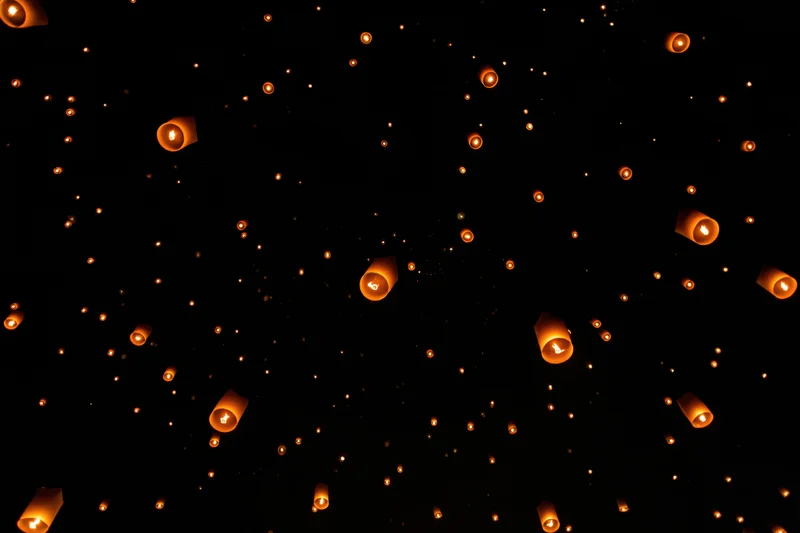 Paper sky lanterns floating upward into the dark night sky