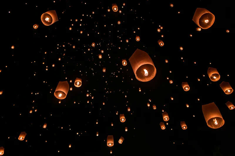 Paper sky lanterns floating upward into the night sky during a festival celebration