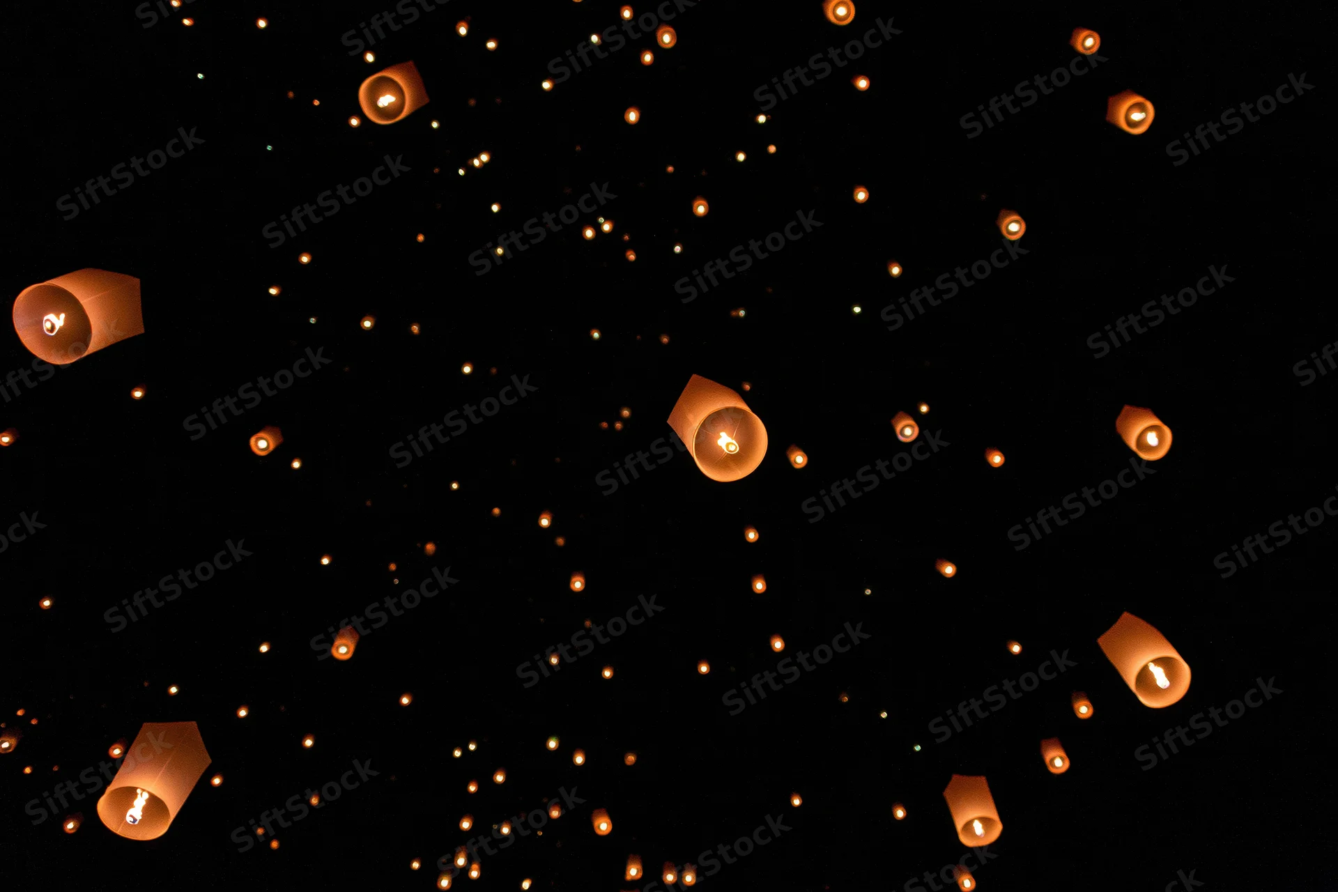 Paper sky lanterns floating upward into the dark night sky