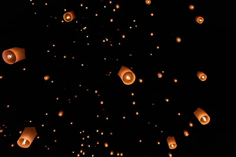 Paper sky lanterns floating upward into the dark night sky