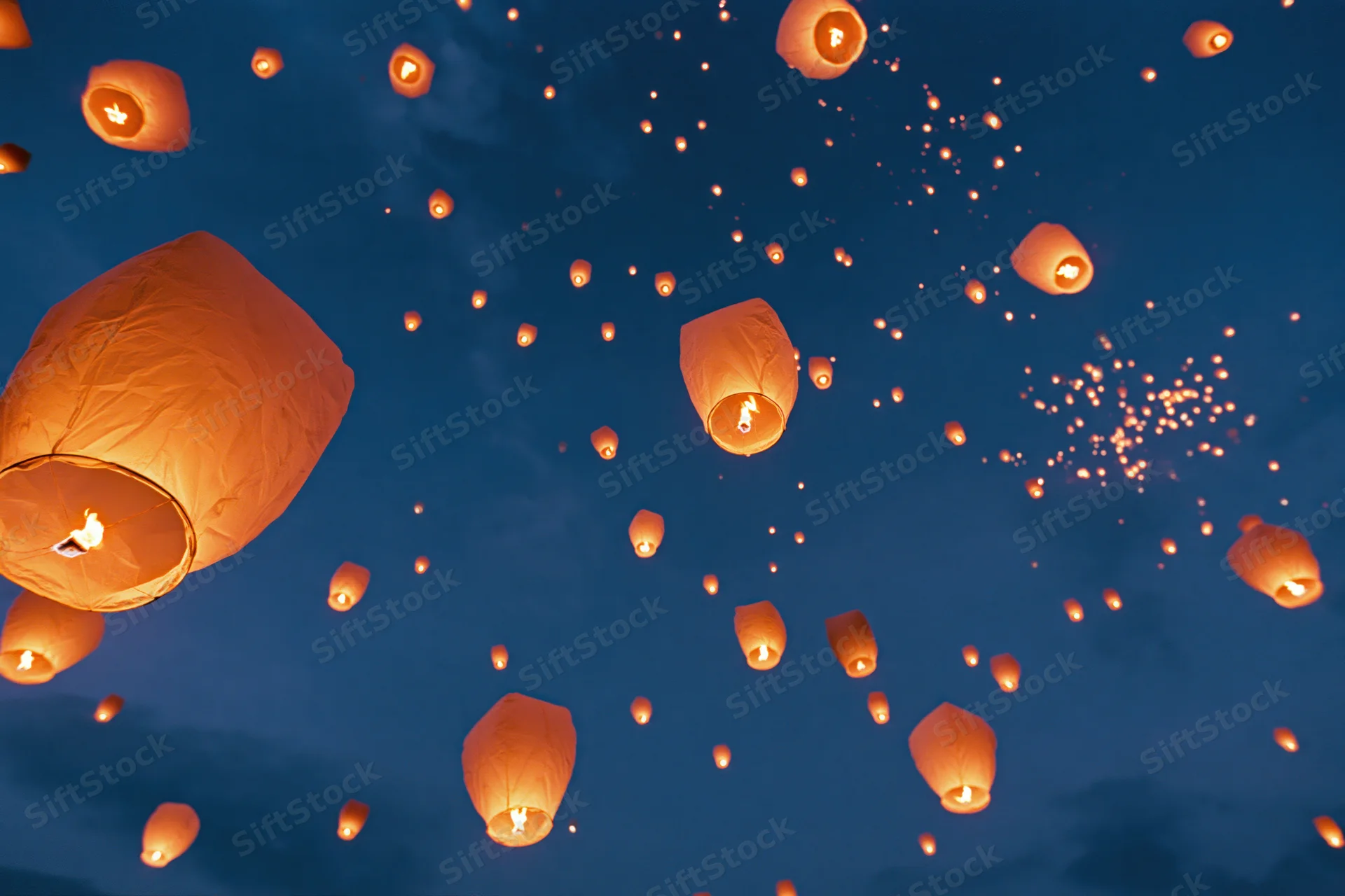 Paper sky lanterns floating upward into the dark blue night sky glowing with orange light