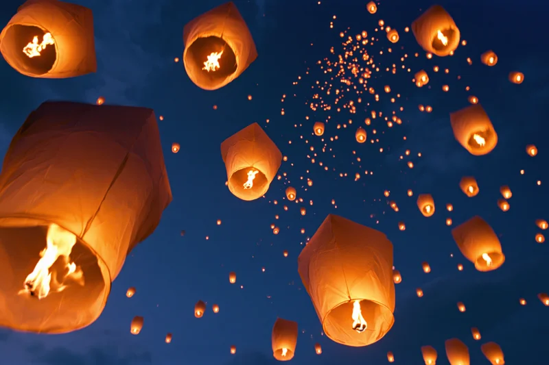 Paper sky lanterns floating upward into the dark night sky glowing with firelight