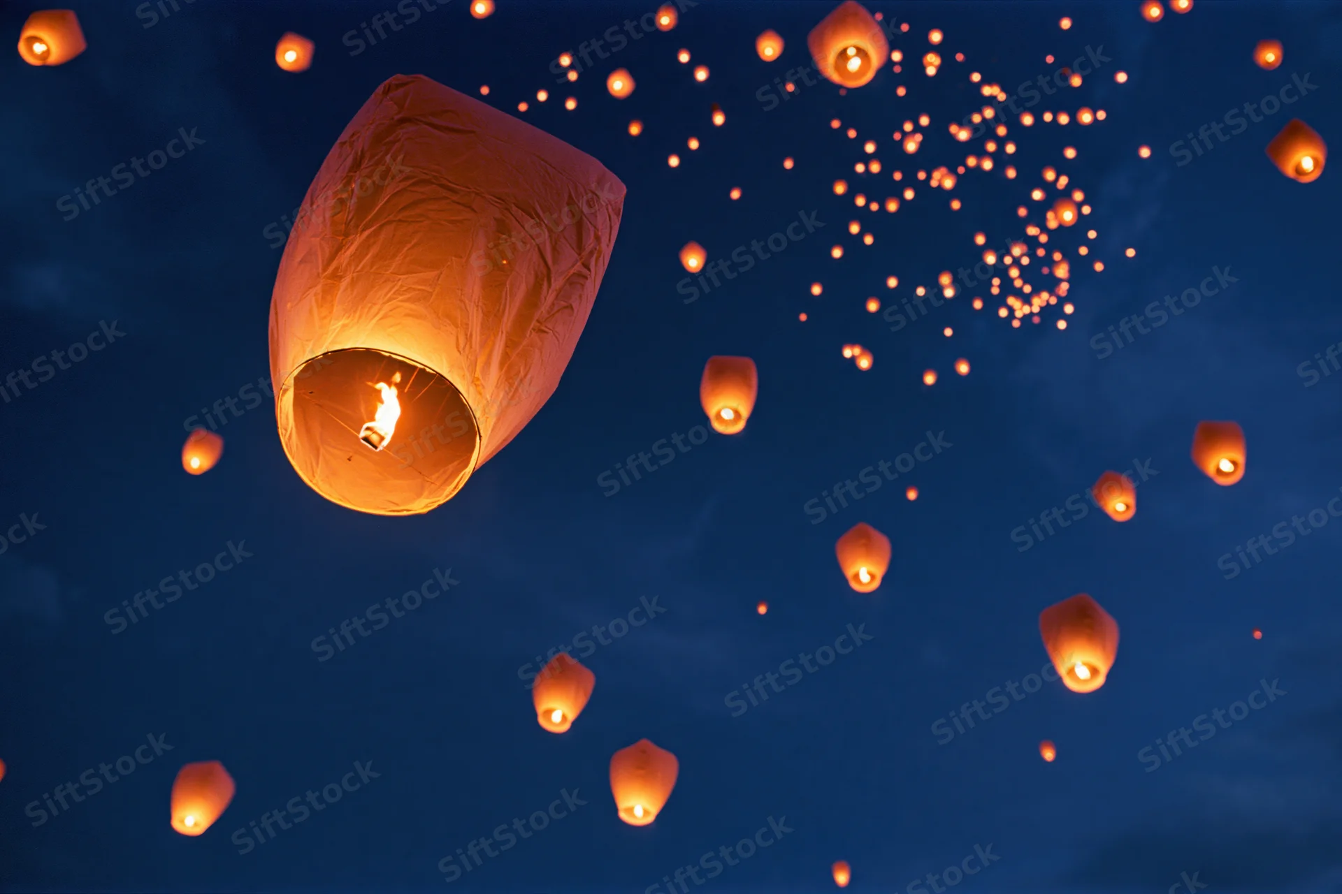 Sky lanterns floating upward into the dark night sky, glowing with warm light from candles inside