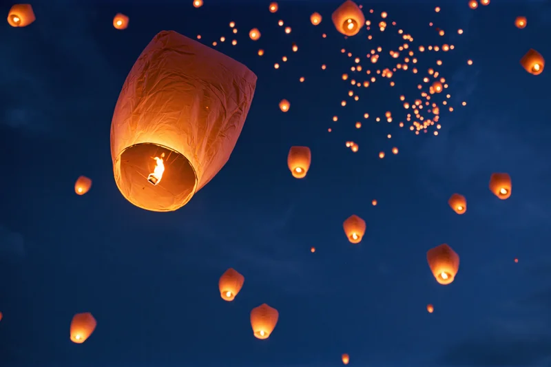 Sky lanterns floating upward into the dark night sky, glowing with warm light from candles inside