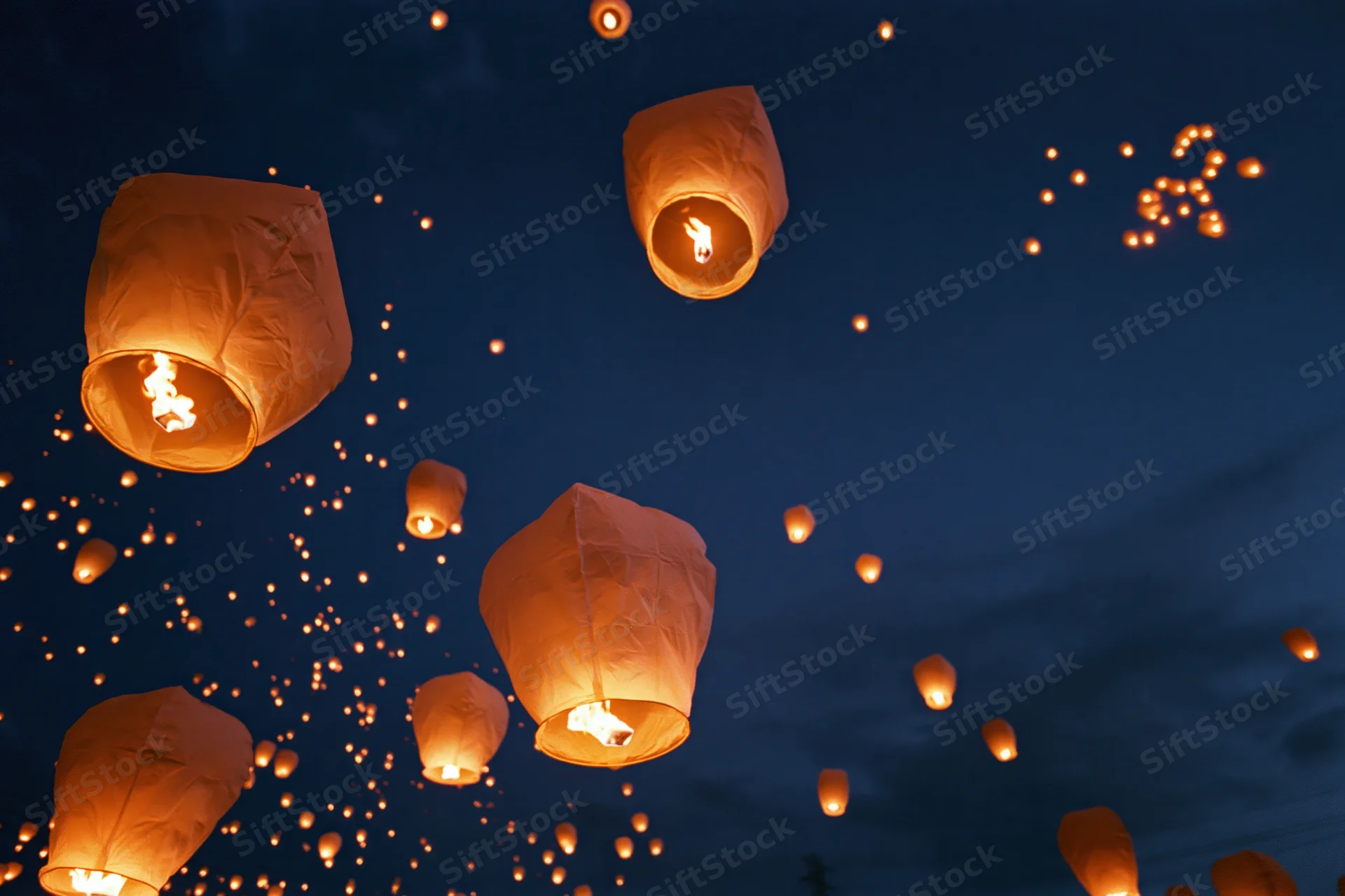 Paper sky lanterns floating upward into the dark night sky glowing with warm light