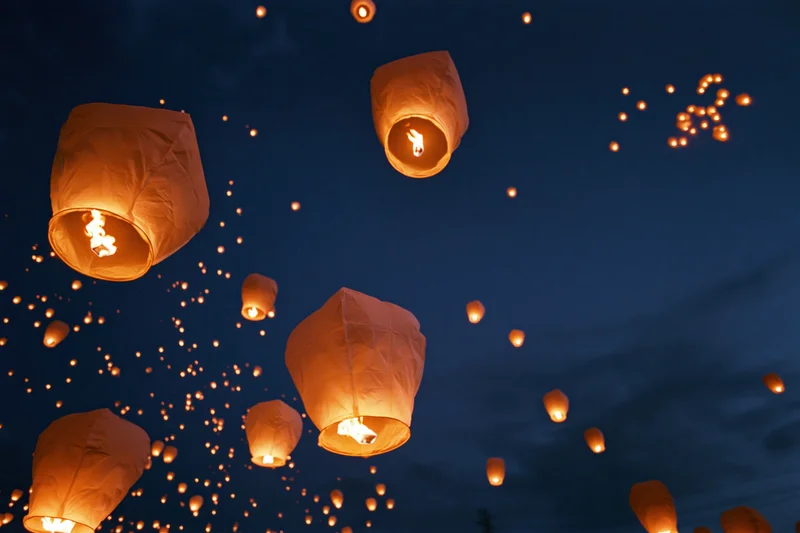 Paper sky lanterns floating upward into the dark night sky glowing with warm light