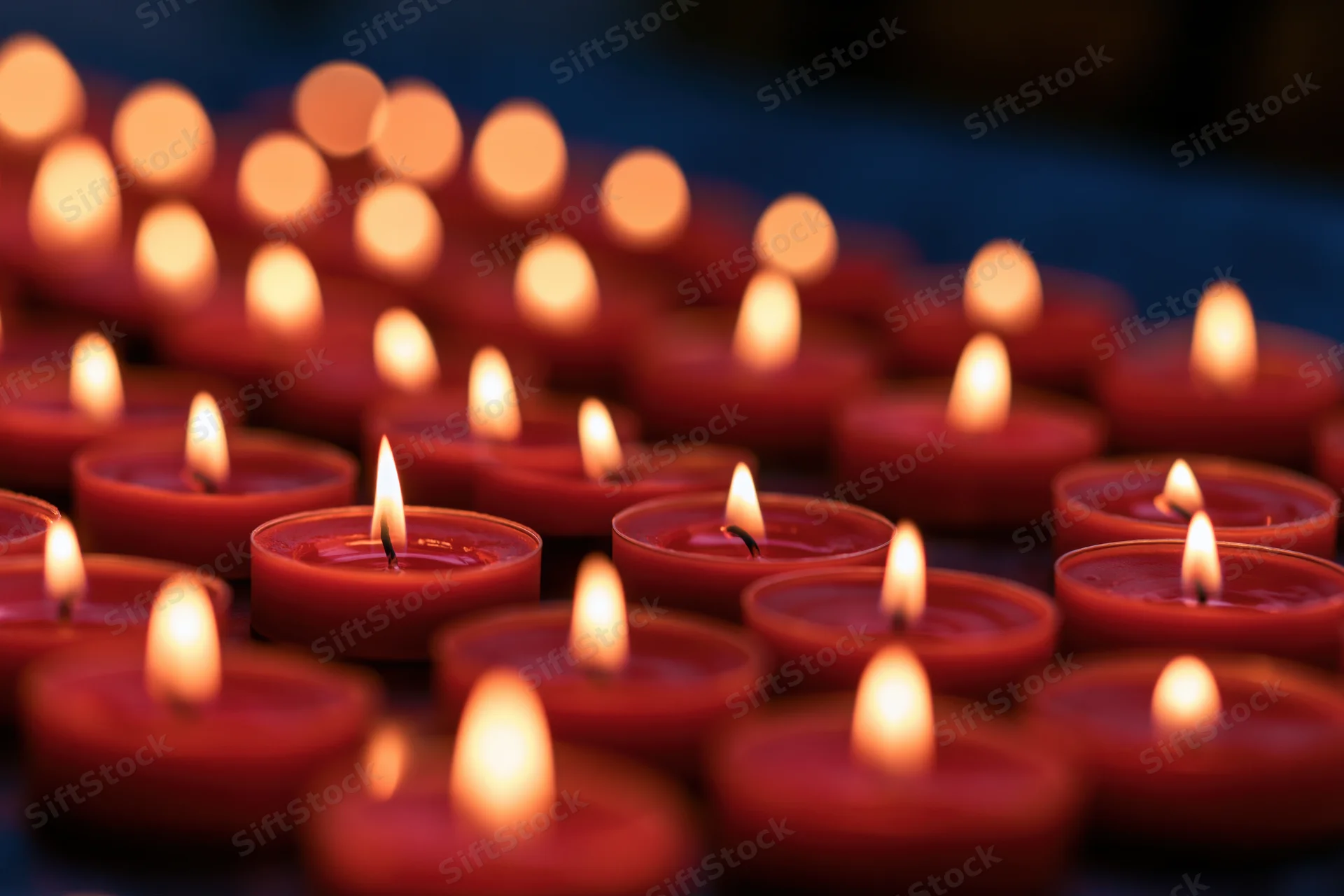 Rows of small red tea light candles burning steadily in dim evening light with soft glow and shallow focus