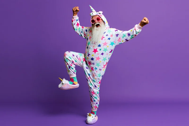 Senior man with white beard in unicorn costume dancing joyfully against purple background