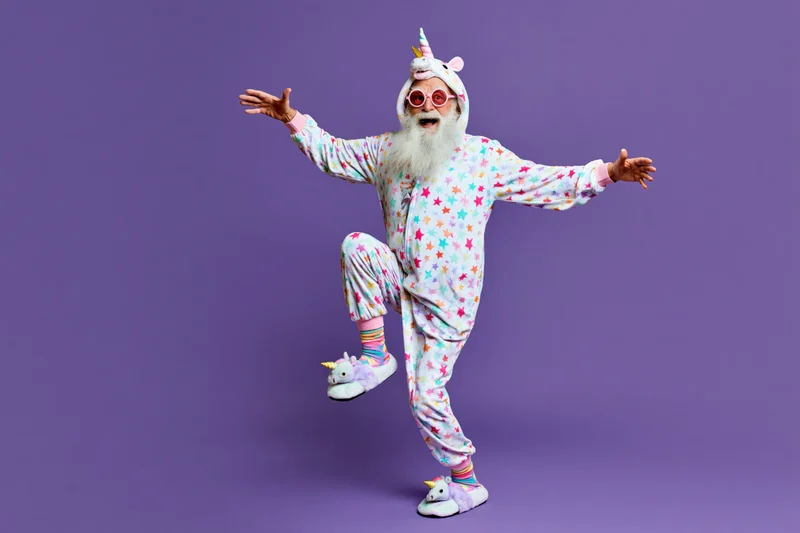 Senior man with white beard dancing in unicorn costume against purple background