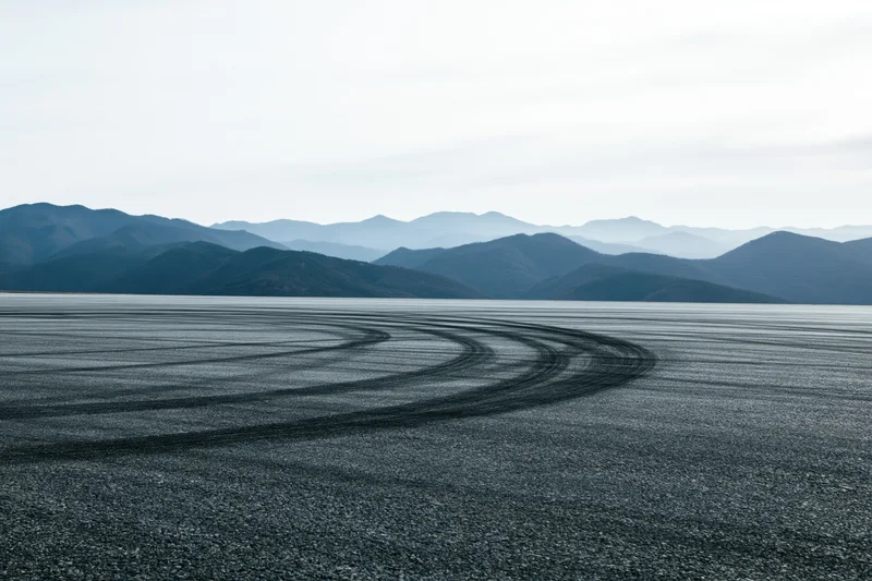 Tire marks curving across an empty asphalt racetrack with mountains in the distance