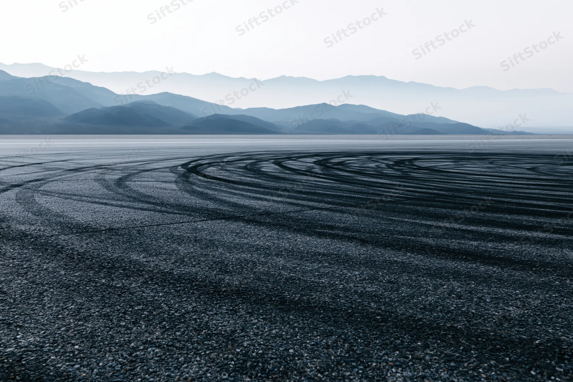 Circular tire tracks on an empty asphalt racing circuit with distant mountains in the background