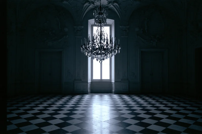 Empty baroque ballroom with ornate plaster moldings and checkered floor lit by a window and chandelier