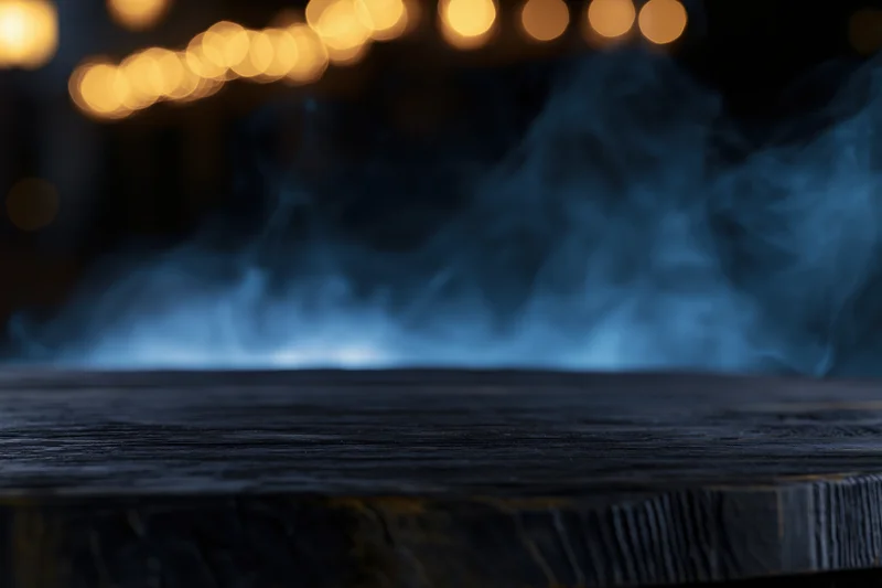 Dark weathered wooden table with blue smoke rising, blurred warm lights in background at night