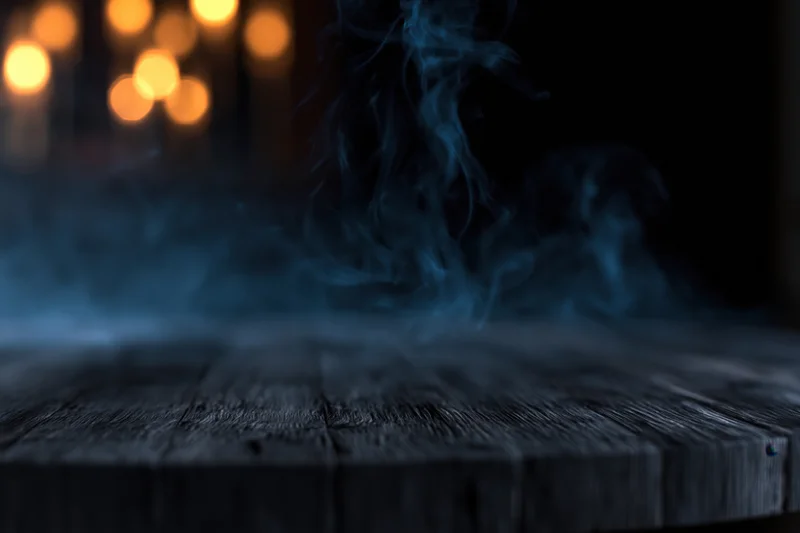 Dark weathered wooden table with rising smoke and blurred warm lights in background
