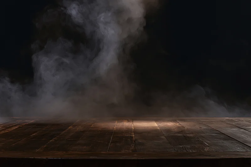 Dark wooden table surface with rising smoke in a dim studio setting