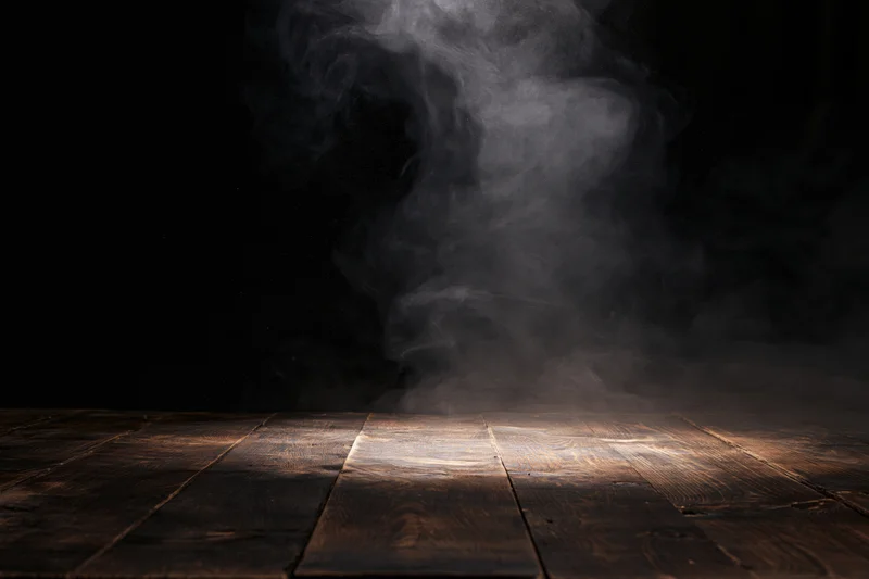 Dark wooden table surface with rising smoke under spotlight, creating moody atmosphere