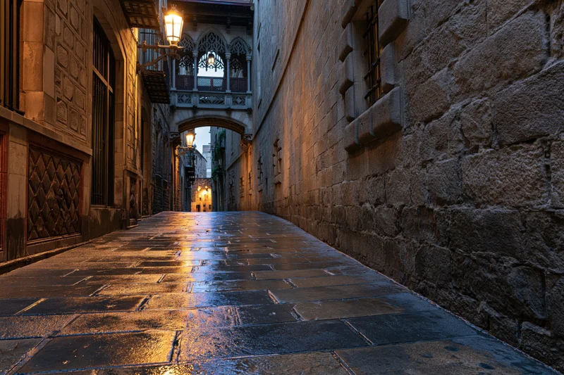 Wet stone alleyway at dusk with glowing lanterns and gothic archway