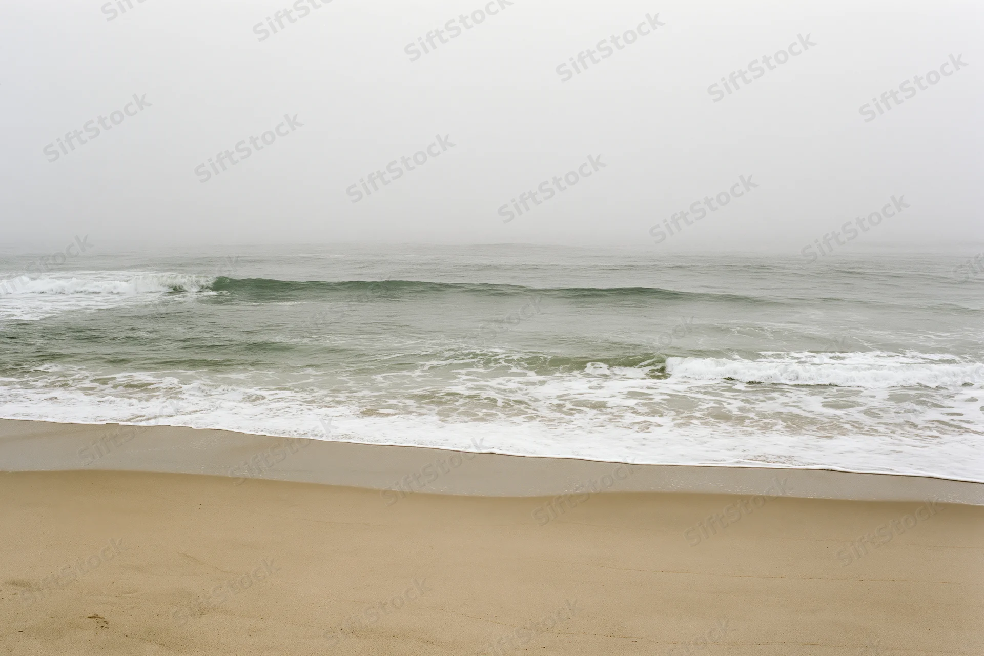 Gentle waves breaking onto a sandy beach under foggy overcast sky