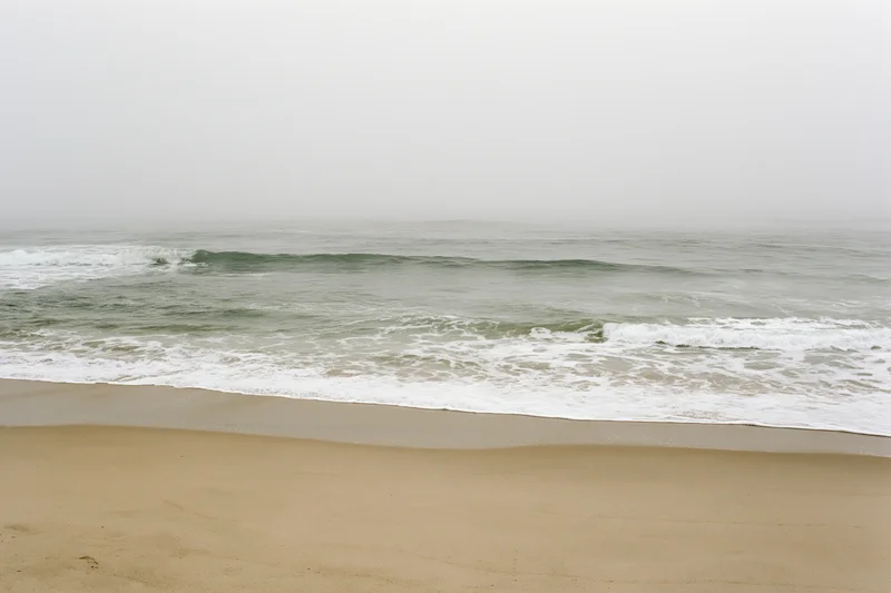 Gentle waves breaking onto a sandy beach under foggy overcast sky