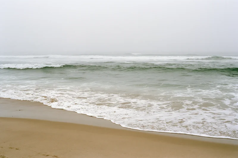Gentle waves breaking onto a sandy beach under an overcast sky