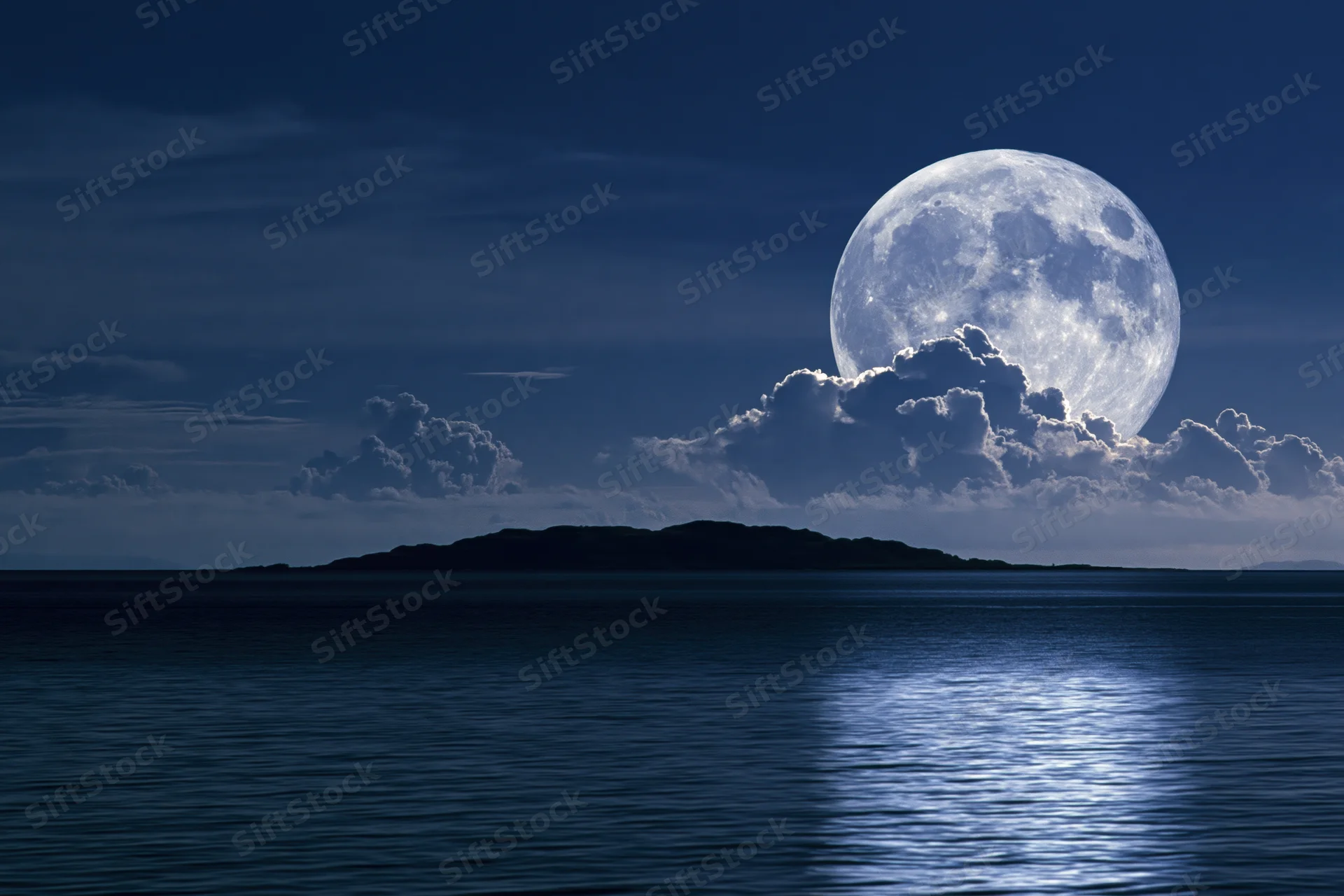 Full moon rising over calm ocean at night with clouds and reflection on water