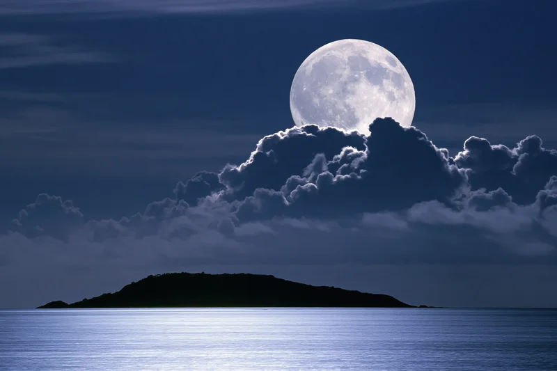 Full moon rising over calm ocean with island silhouette at night
