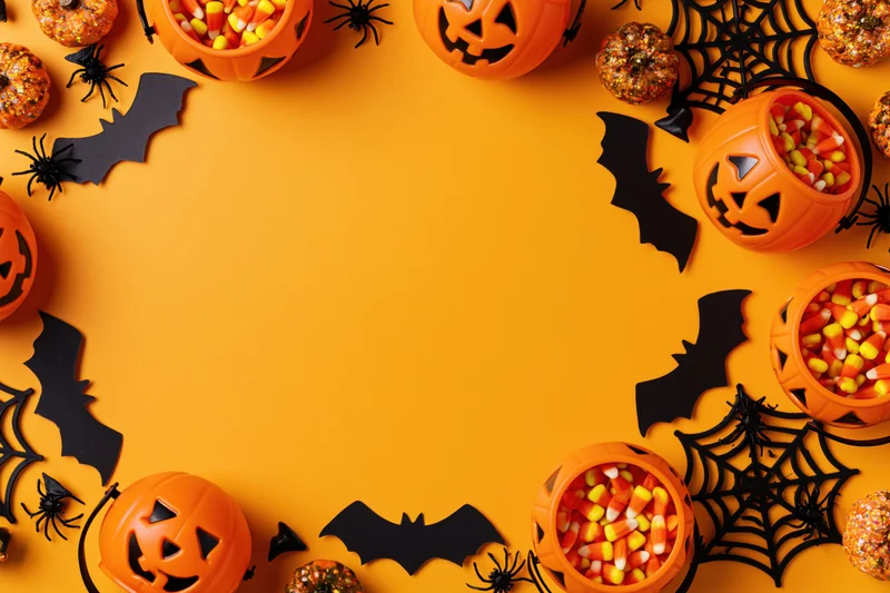 Halloween decorations and candy arranged in a circular frame on orange background with copyspace