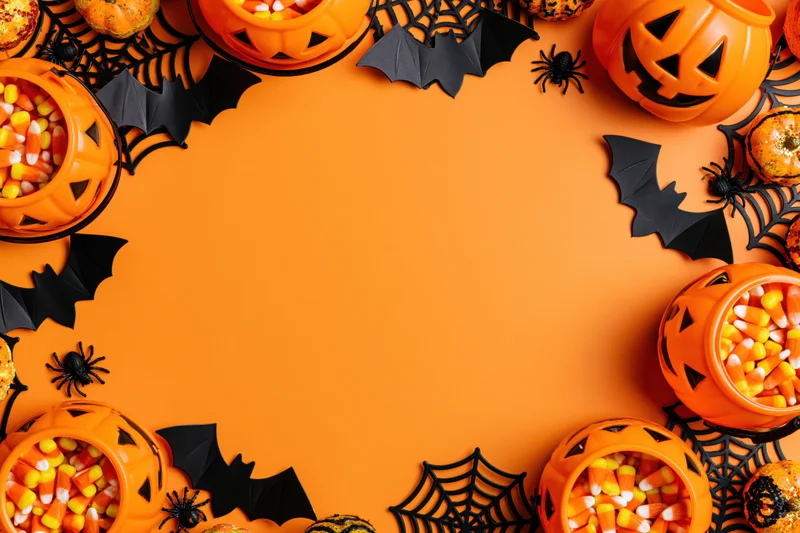 Halloween decorations and candy arranged in a circular frame on orange background with copyspace