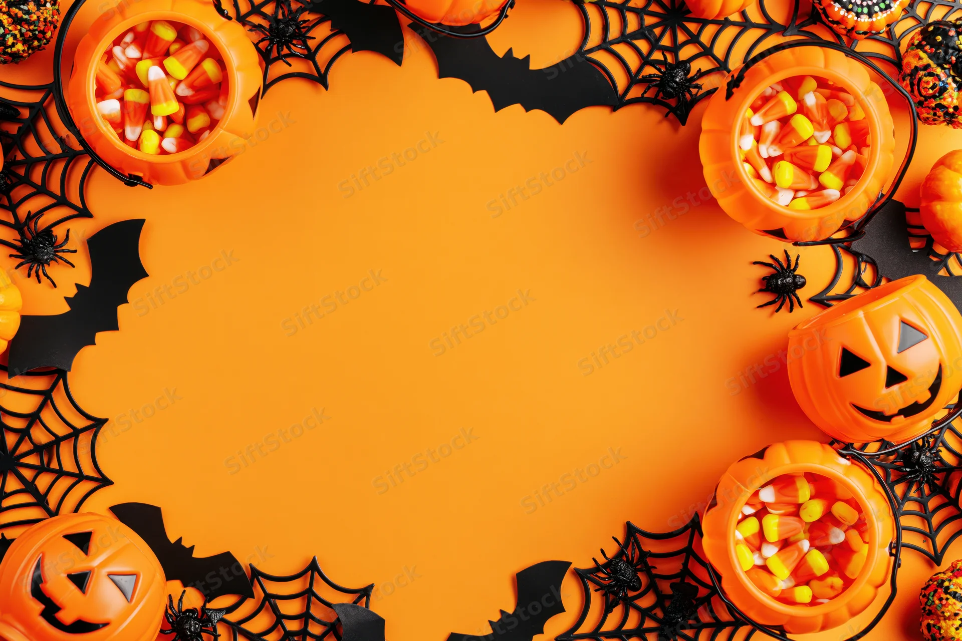 Halloween decorations and candy arranged in a circular border on orange background with copyspace