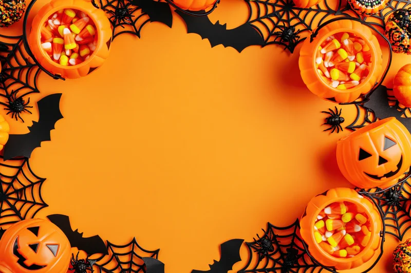 Halloween decorations and candy arranged in a circular border on orange background with copyspace