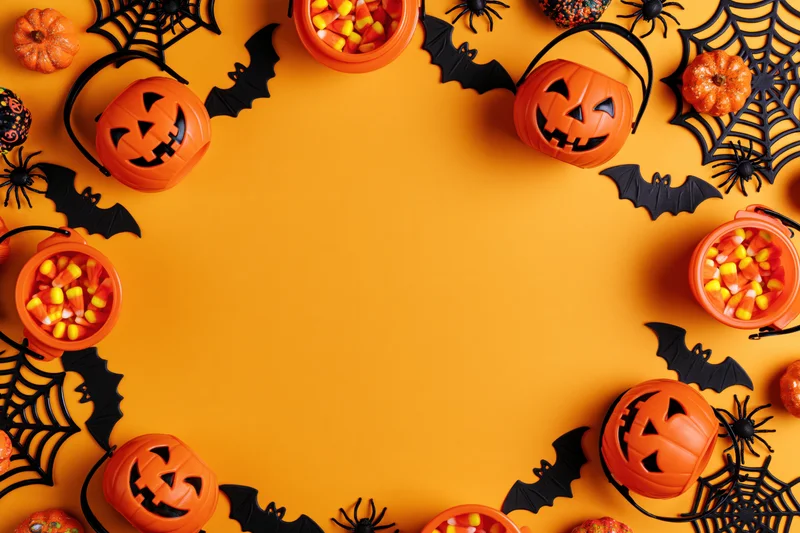 Halloween decorations and candy arranged in a circular frame on orange background with copyspace