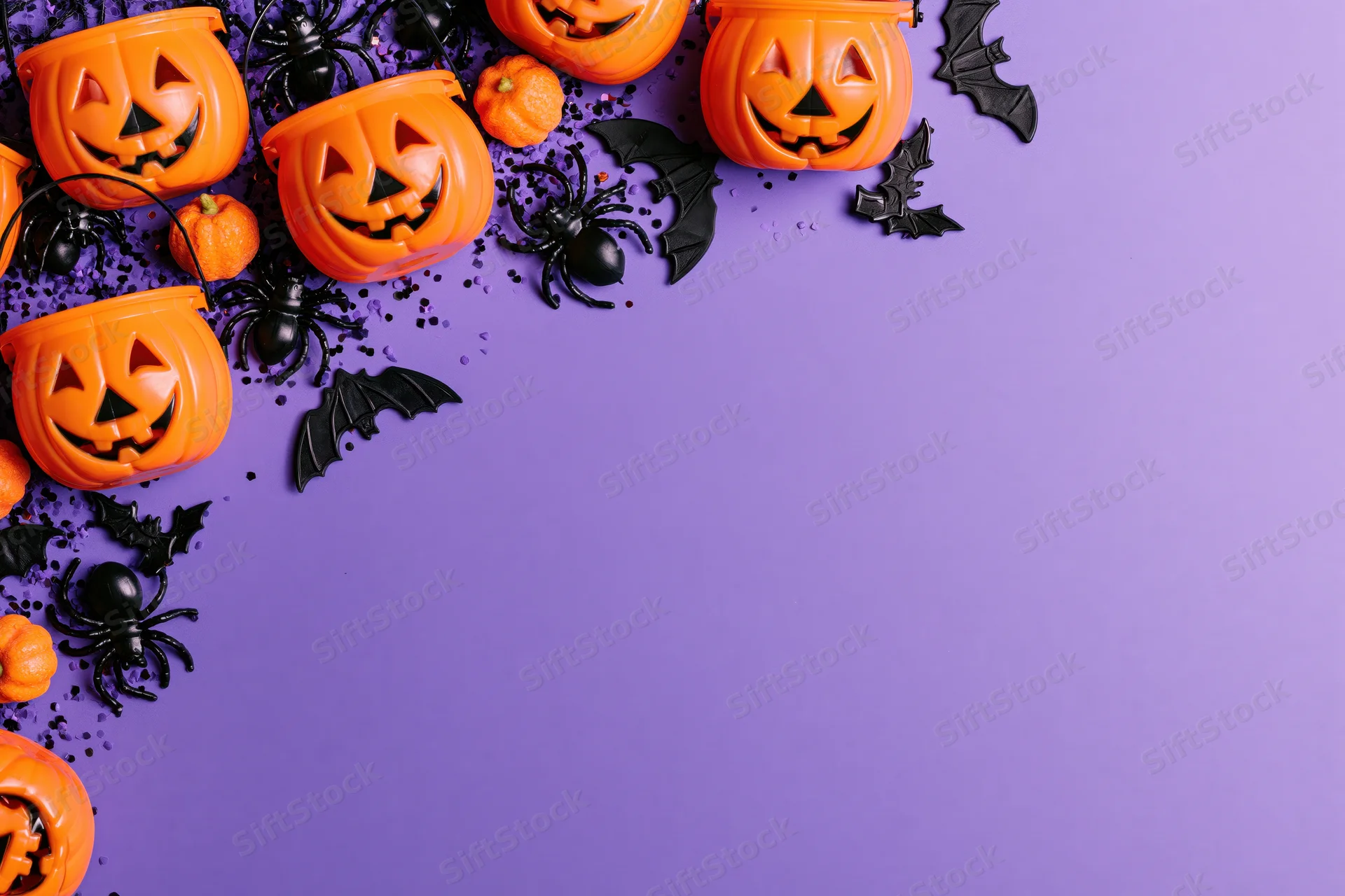 Orange plastic jack-o-lantern candy buckets and black spiders bats arranged on purple surface with copyspace