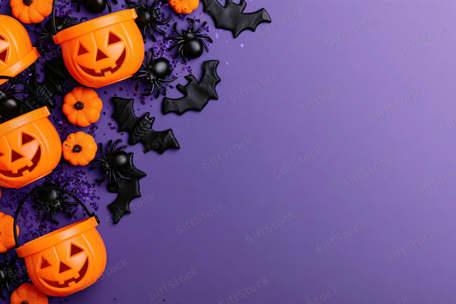 Orange plastic jack-o-lantern candy buckets and black bats spiders arranged on purple surface for halloween flat lay