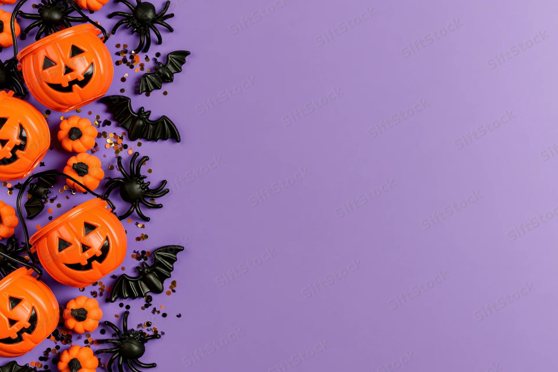 Orange plastic jack-o-lantern candy buckets and black spiders bats on purple surface with copyspace